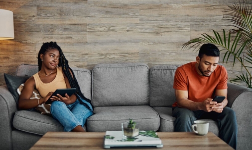 Couple sitting on different ends of a couch on technology.