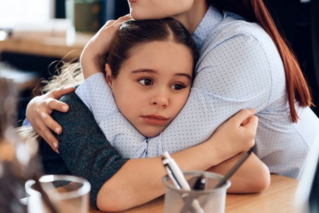 Young sad mother hugs little upset daughter sitting in lawyer's office for divorce.