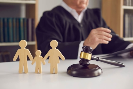 Gavel, sound block and small wooden figurines of husband, wife and kid on judge's table.